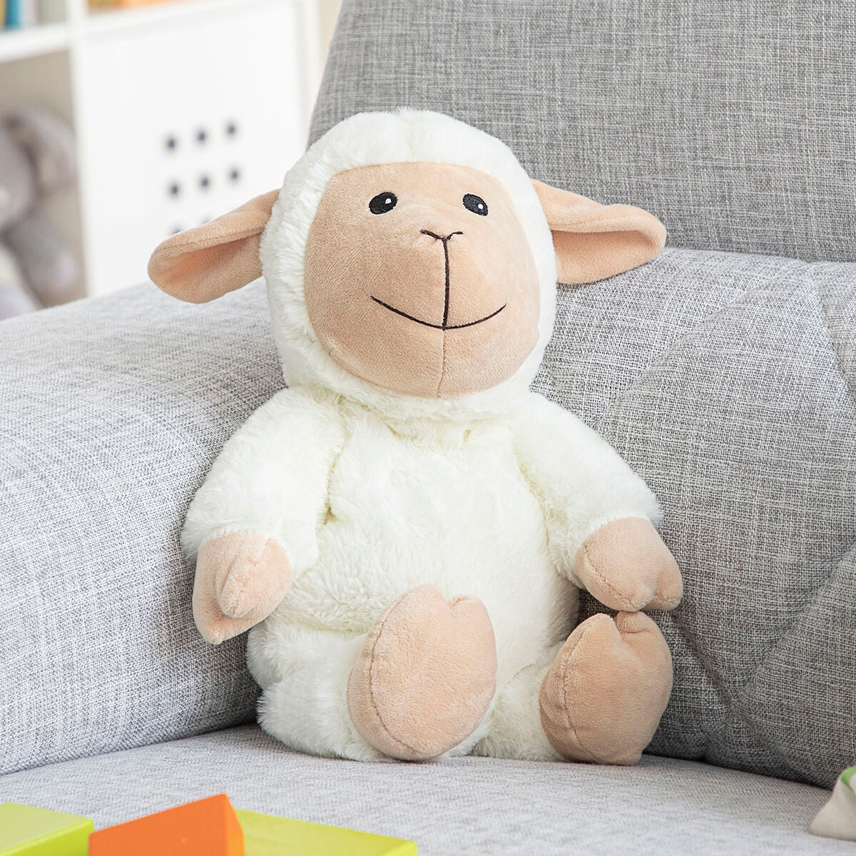 Sheep Soft Toy with Warming and Cooling Effect Wooly InnovaGoods sitting on a couch with colorful toys.