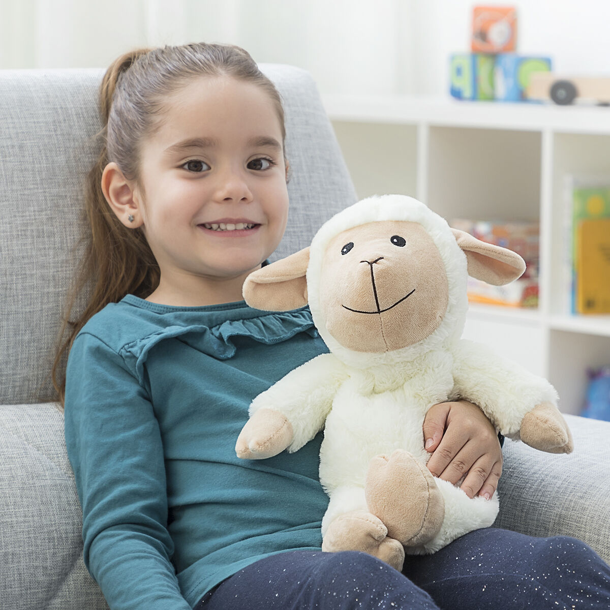 Girl holding Sheep Soft Toy with Warming and Cooling Effect Wooly InnovaGoods, smiling in cozy setting.